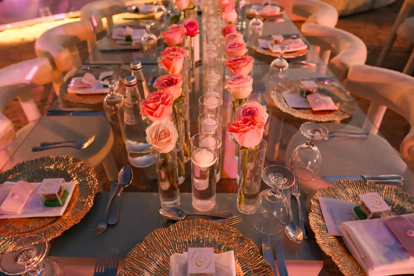 Intimate table setting with pink roses in glass vases and gold charger plates at desert wedding