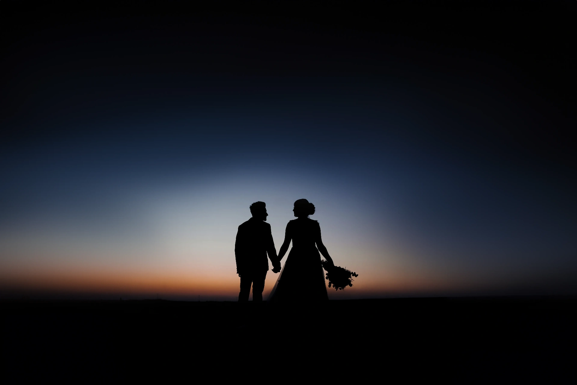 Bride and groom silhouette holding hands against a glowing sunset sky in Dubai desert