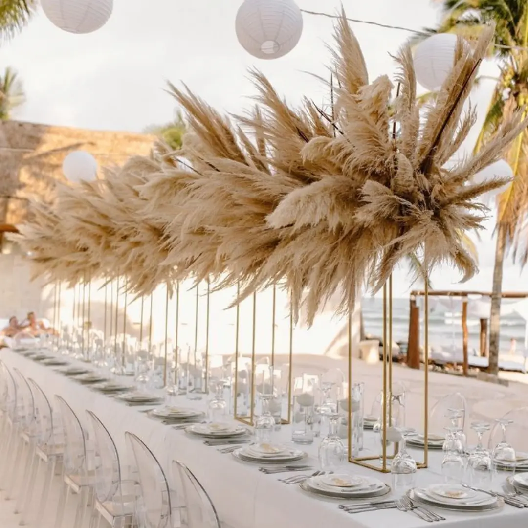 Luxury beachside wedding table with pampas grass centerpieces and ghost chairs at golden hour