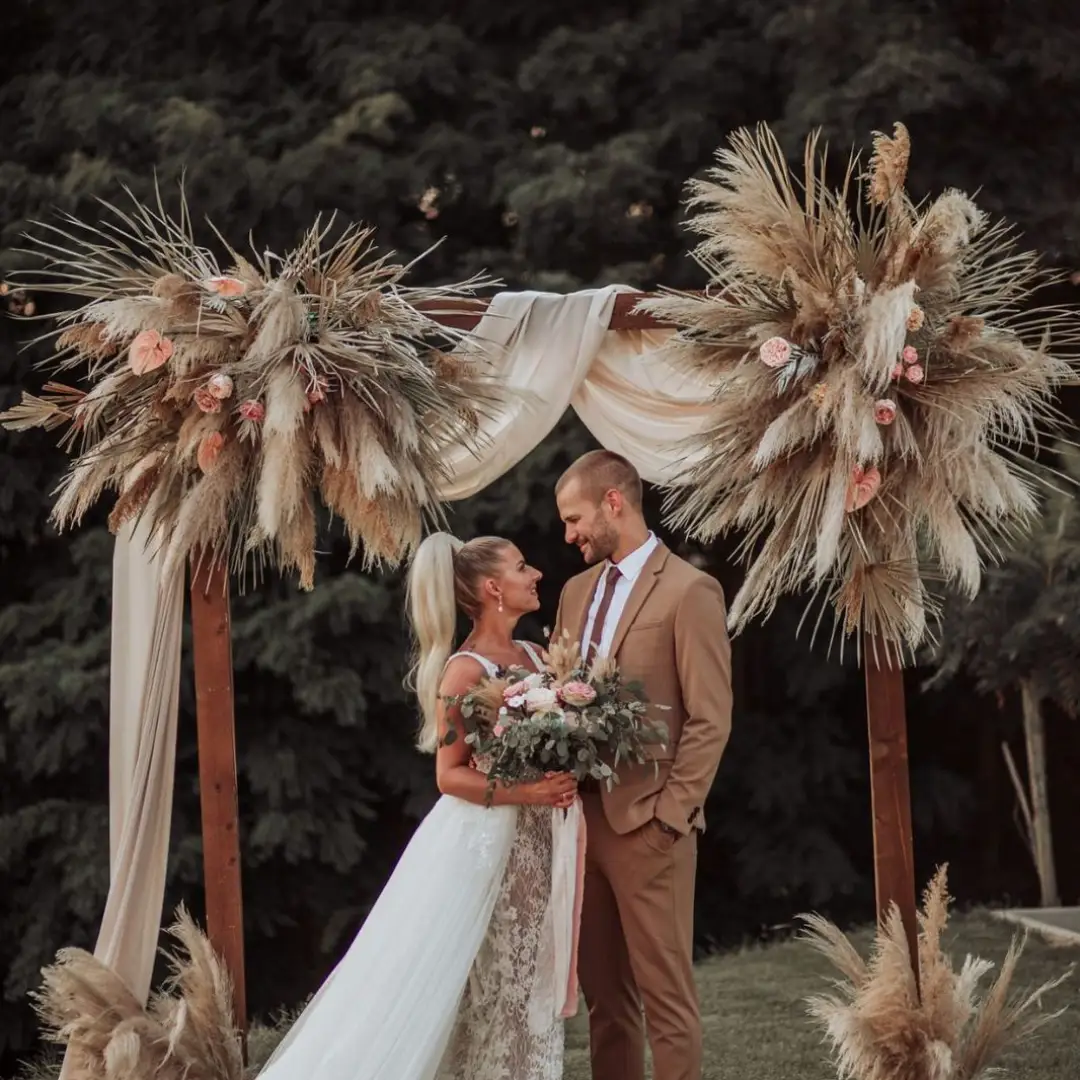 Bride and groom under a bohemian pampas grass and draped fabric wedding arch