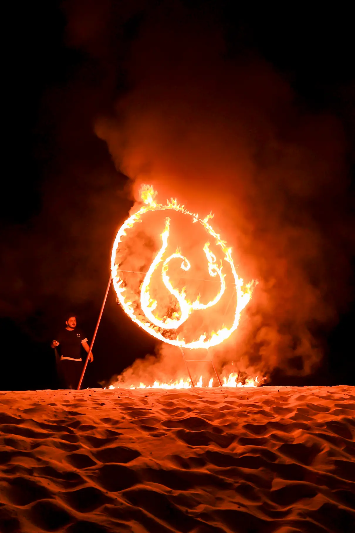 Dramatic fire performer spinning a name on fire on desert sand at night