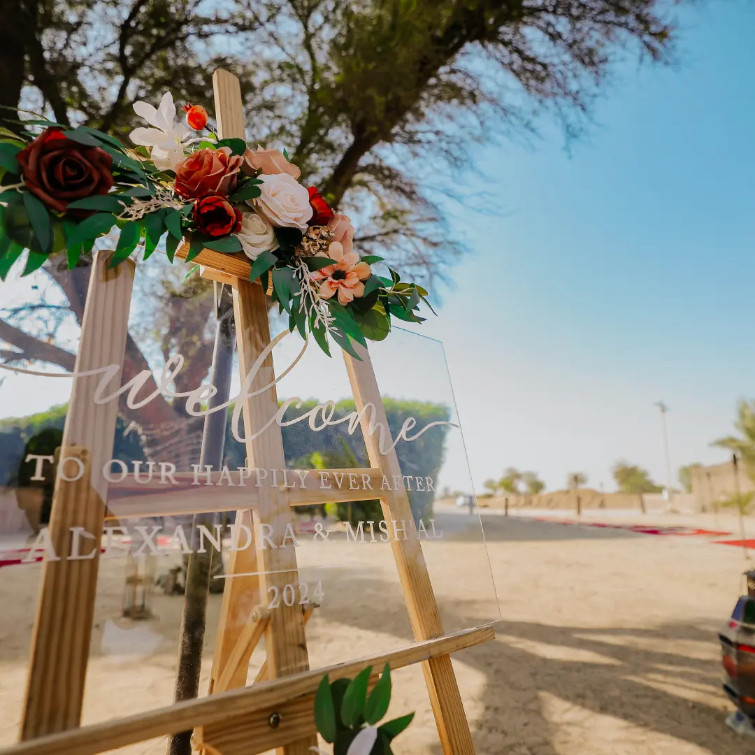 Acrylic welcome sign with floral garland on wooden easel at a desert wedding venue