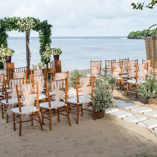 Beachfront wedding ceremony setup with chiavari chairs, tulle sashes, and lush floral arrangements overlooking the ocean