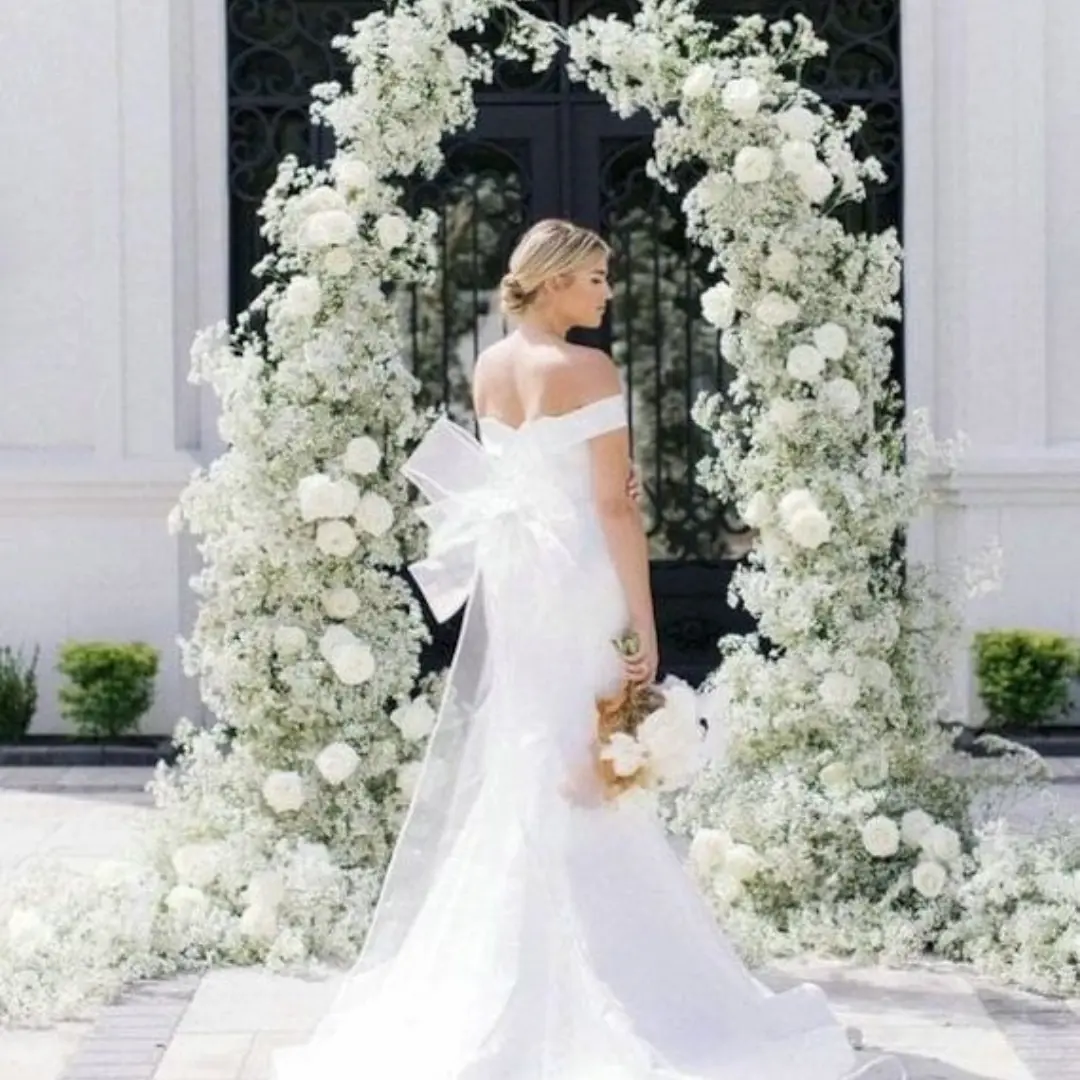 Bride in white gown standing under a grand white floral arch at luxury wedding venue